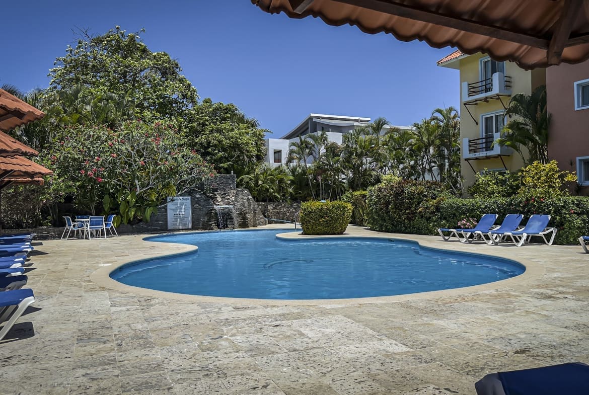 buyDRproperty Swimming pool surrounded by lounge chairs under umbrellas at a resort Sosua Real Estate