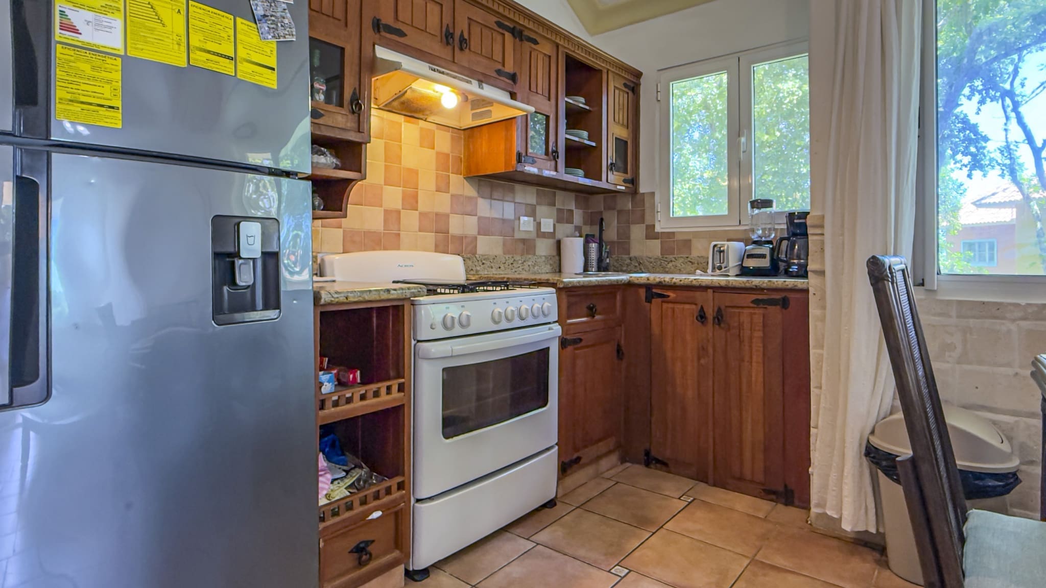 Cozy kitchen with a stainless refrigerator, white oven, granite counters, and warm wooden cabinets under a tiled backsplash.