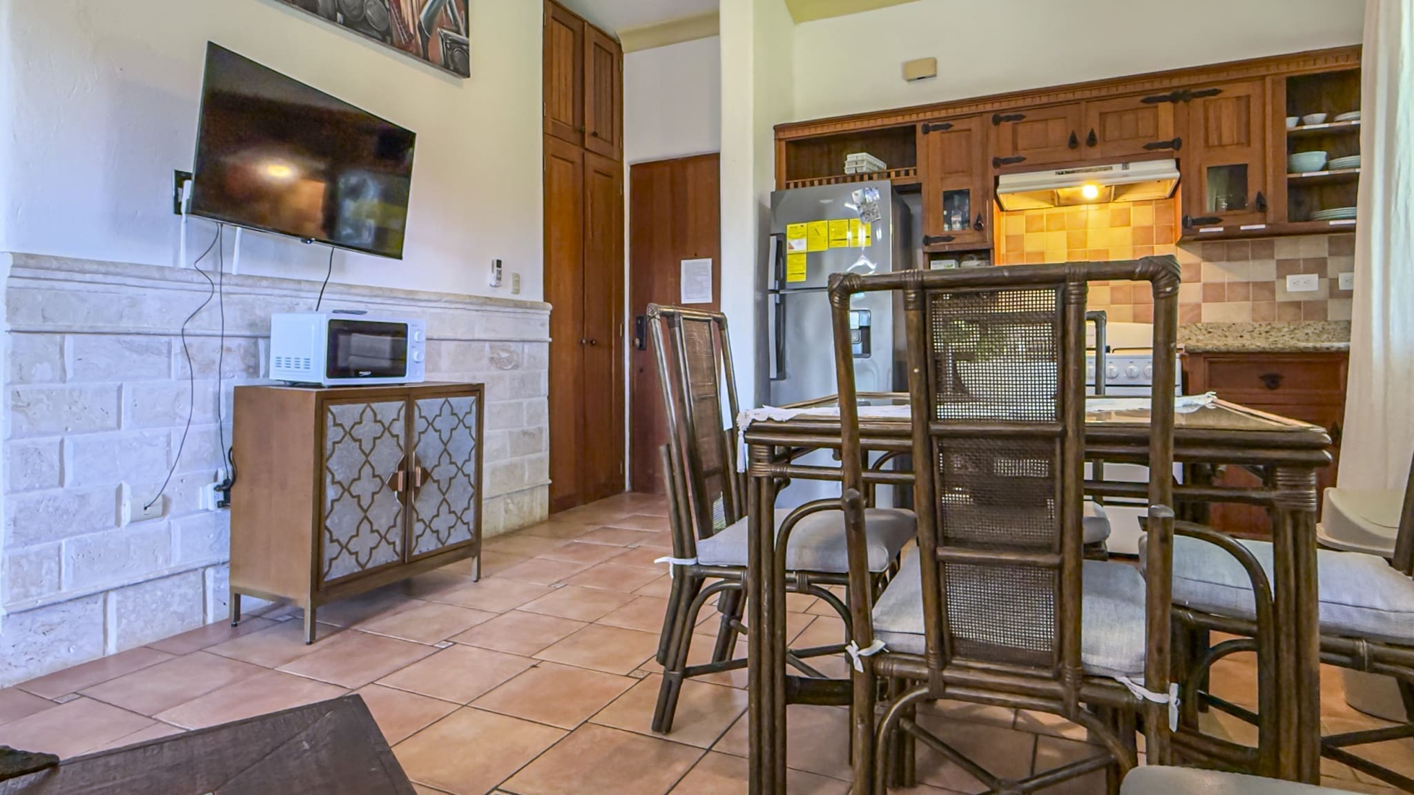 buyDRproperty Dining area with wicker chairs and table, kitchen with wooden cabinets, and a microwave. Sosua Real Estate