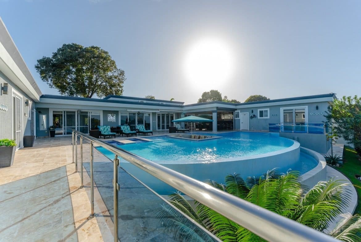 buyDRproperty Luxury villa with a large, modern swimming pool and lounge area on a sunny day. Sosua Real Estate