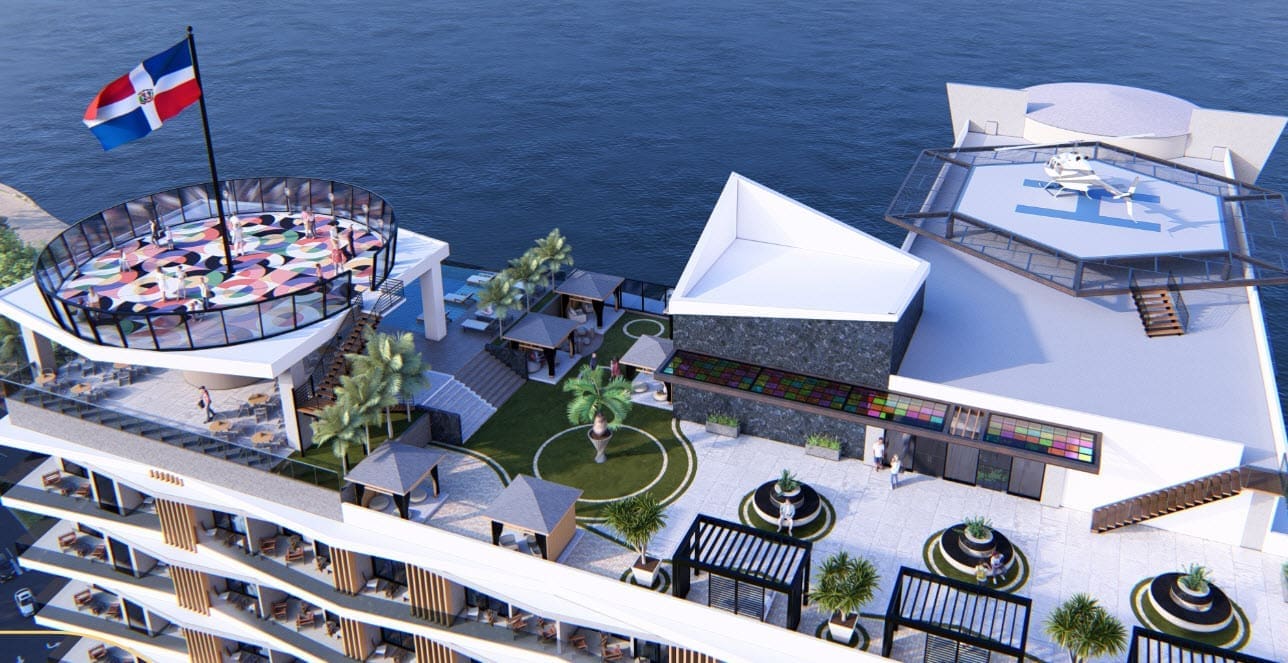 Aerial view of a modern rooftop resort by the ocean, featuring a circular glass-rail deck, palm trees, colorful seating, and a helipad.