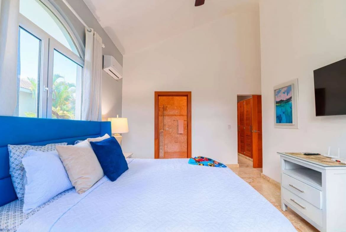 buyDRproperty Bright bedroom with a blue headboard, white bedding, and large arched window. Sosua Real Estate