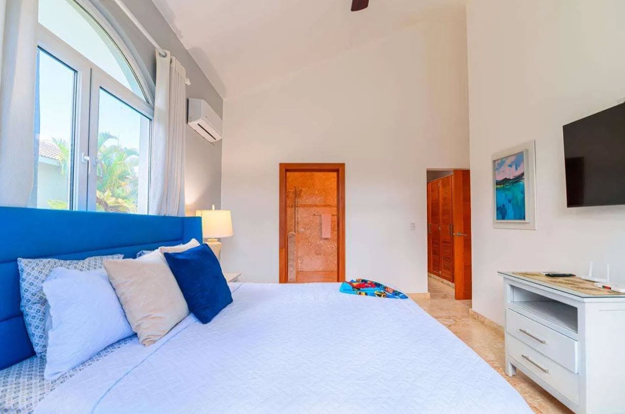 buyDRproperty Bright bedroom with a blue headboard, white bedding, and large arched window. Sosua Real Estate