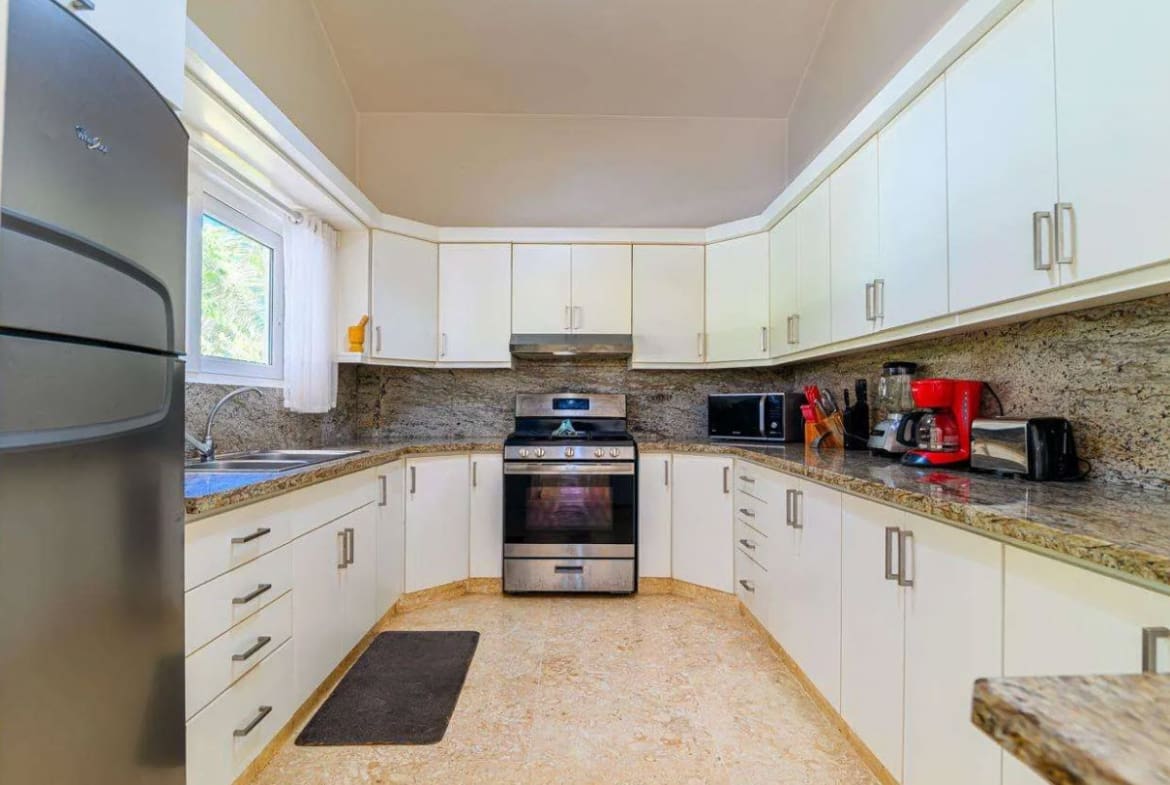 buyDRproperty Modern white kitchen with granite countertops, stainless steel appliances, and a window. Sosua Real Estate