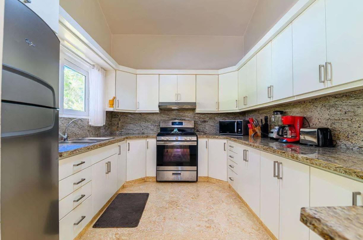 buyDRproperty Modern white kitchen with granite countertops, stainless steel appliances, and a window. Sosua Real Estate