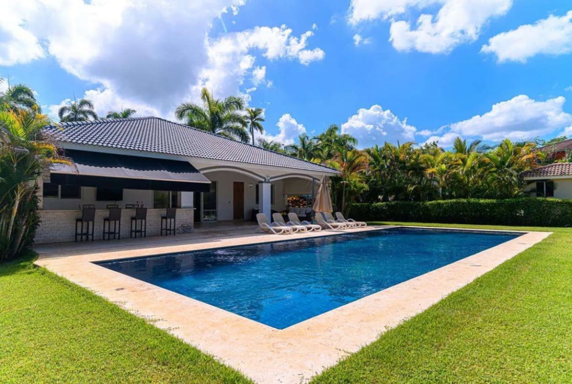 buyDRproperty Luxurious backyard with a large swimming pool, covered bar, and lush green lawn. Sosua Real Estate