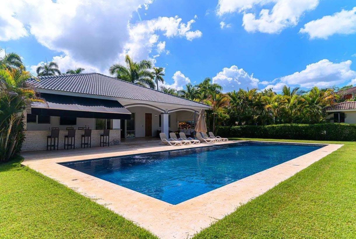 buyDRproperty Luxurious backyard with a large swimming pool, covered bar, and lush green lawn. Sosua Real Estate