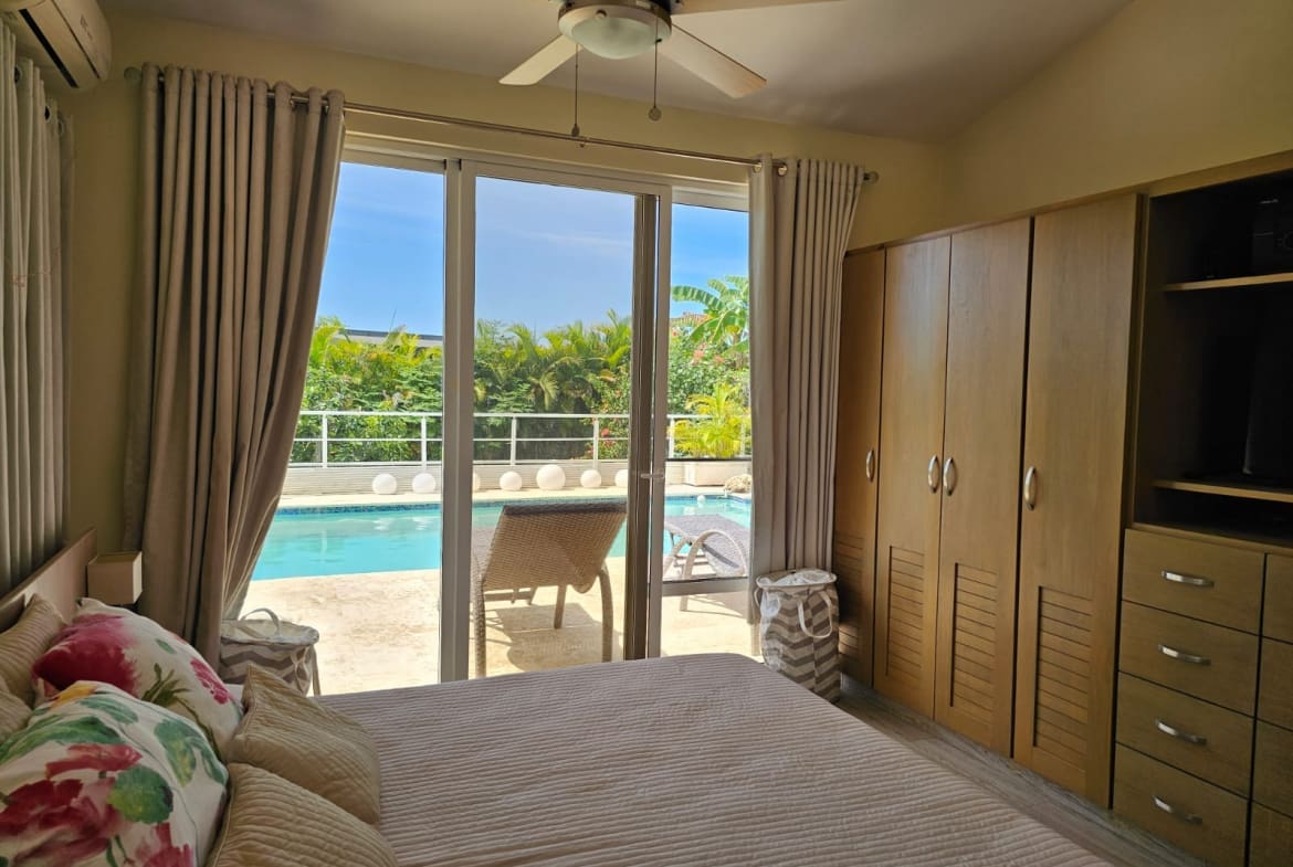 buyDRproperty Bedroom with tropical pool view, ceiling fan, and wooden wardrobe Sosua Real Estate