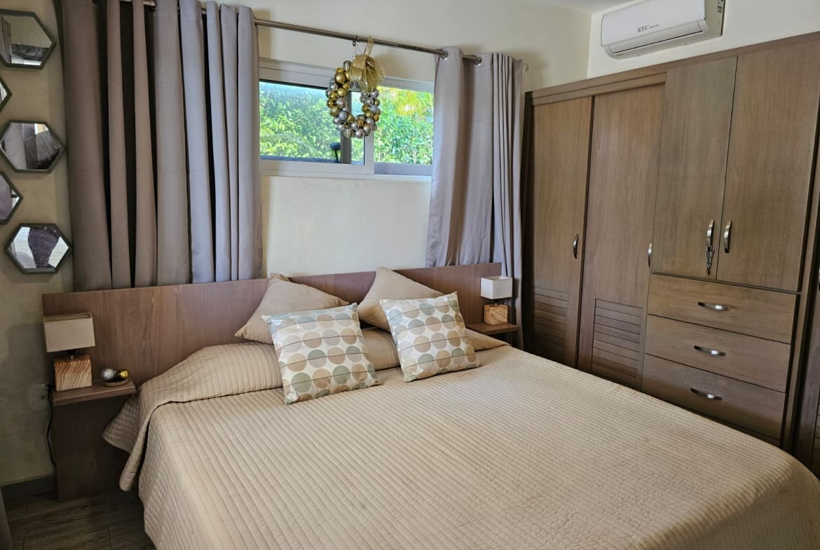 buyDRproperty Cozy bedroom with a queen-size bed, wooden wardrobe, and window decor. Sosua Real Estate