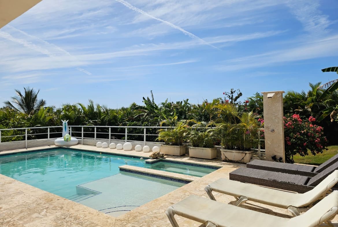 buyDRproperty Luxury villa pool with lounge chairs and tropical foliage under a blue sky. Sosua Real Estate