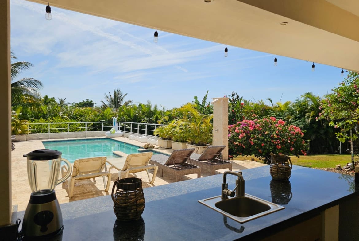 buyDRproperty Outdoor kitchen bar with sink and blender overlooking a tropical pool and lounge area. Sosua Real Estate