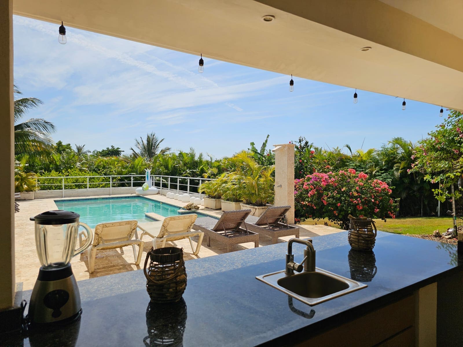 buyDRproperty Outdoor kitchen bar with sink and blender overlooking a tropical pool and lounge area. Sosua Real Estate