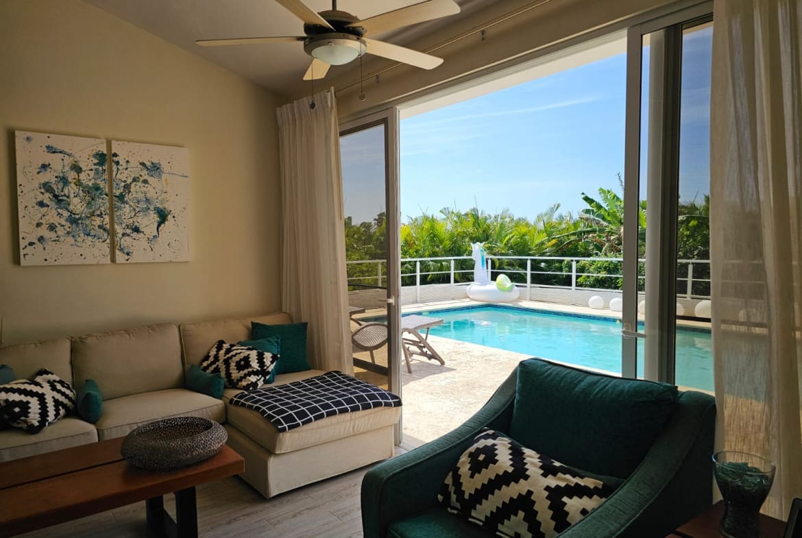 buyDRproperty Living room with sofa and armchair opens to a tropical pool patio with a unicorn float. Sosua Real Estate