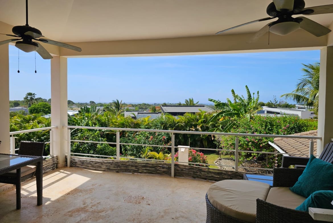 buyDRproperty Spacious balcony with ceiling fans, outdoor seating, and lush tropical garden view. Sosua Real Estate