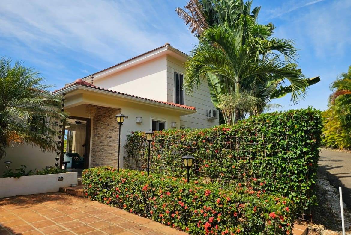 buyDRproperty Tropical villa entrance with lush greenery and red flowers Sosua Real Estate
