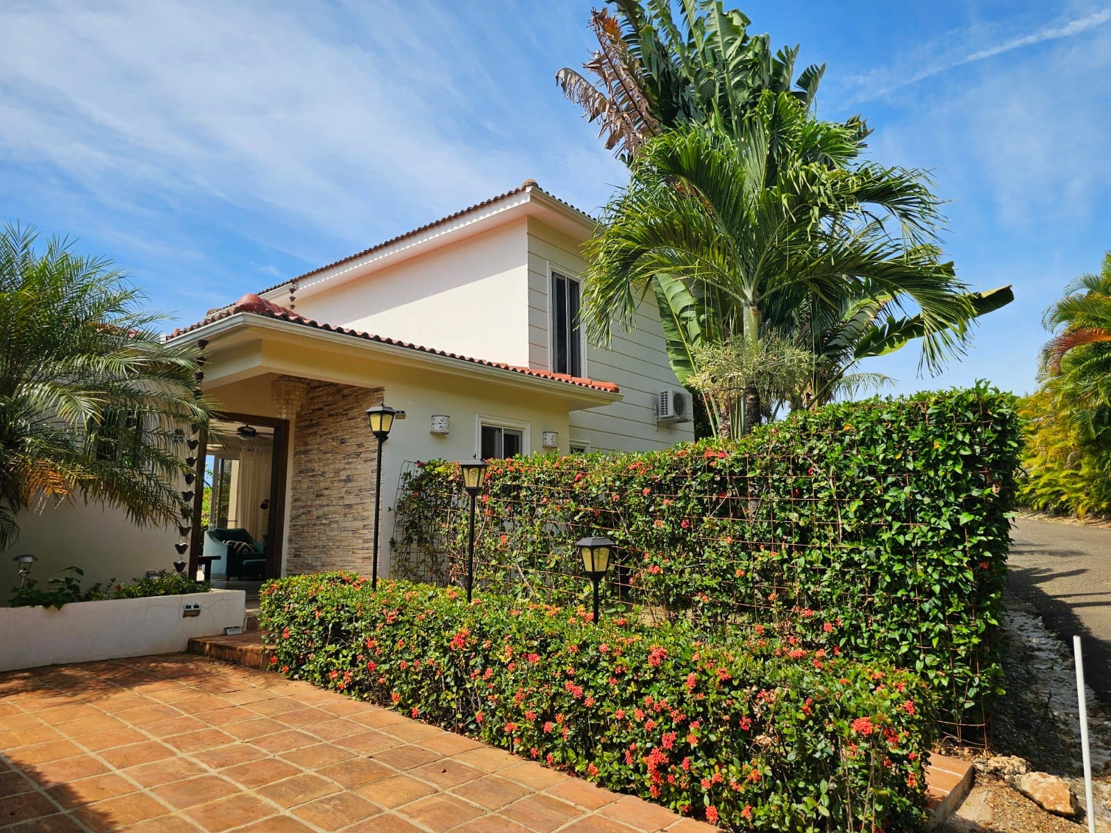 buyDRproperty Tropical villa entrance with lush greenery and red flowers Sosua Real Estate