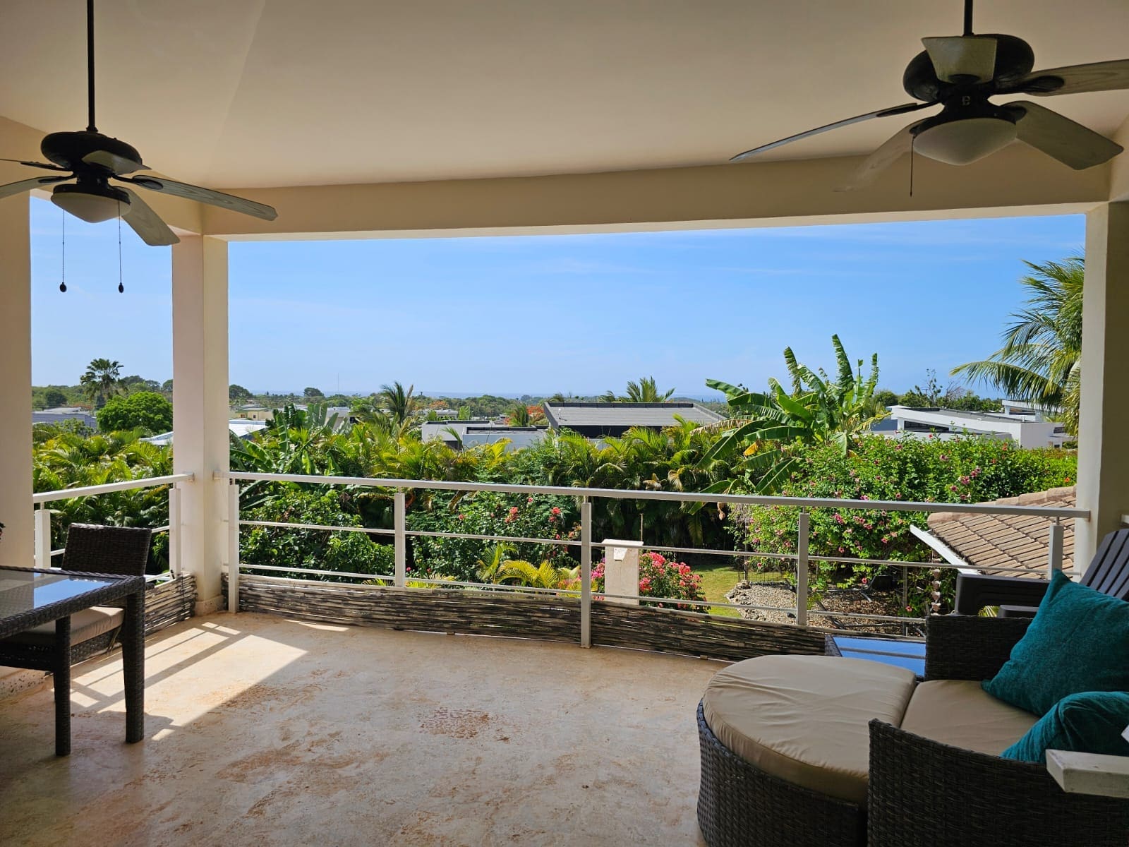 buyDRproperty Spacious balcony with ceiling fans, outdoor seating, and lush tropical garden view. Sosua Real Estate