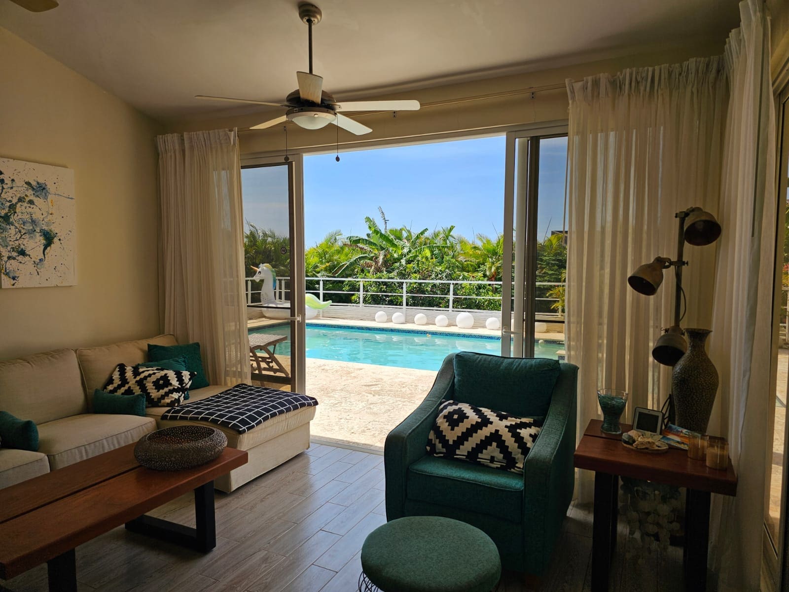 buyDRproperty Living room with teal armchair and sofa opens to a bright blue swimming pool and tropical greenery. Sosua Real Estate