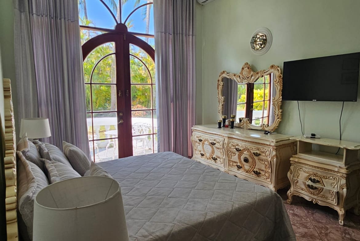 buyDRproperty Bedroom with arched window, ornate dresser, and tropical garden view Sosua Real Estate