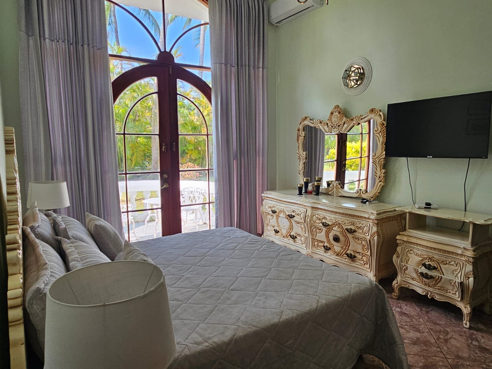 buyDRproperty Bedroom with arched window, ornate dresser, and tropical garden view Sosua Real Estate