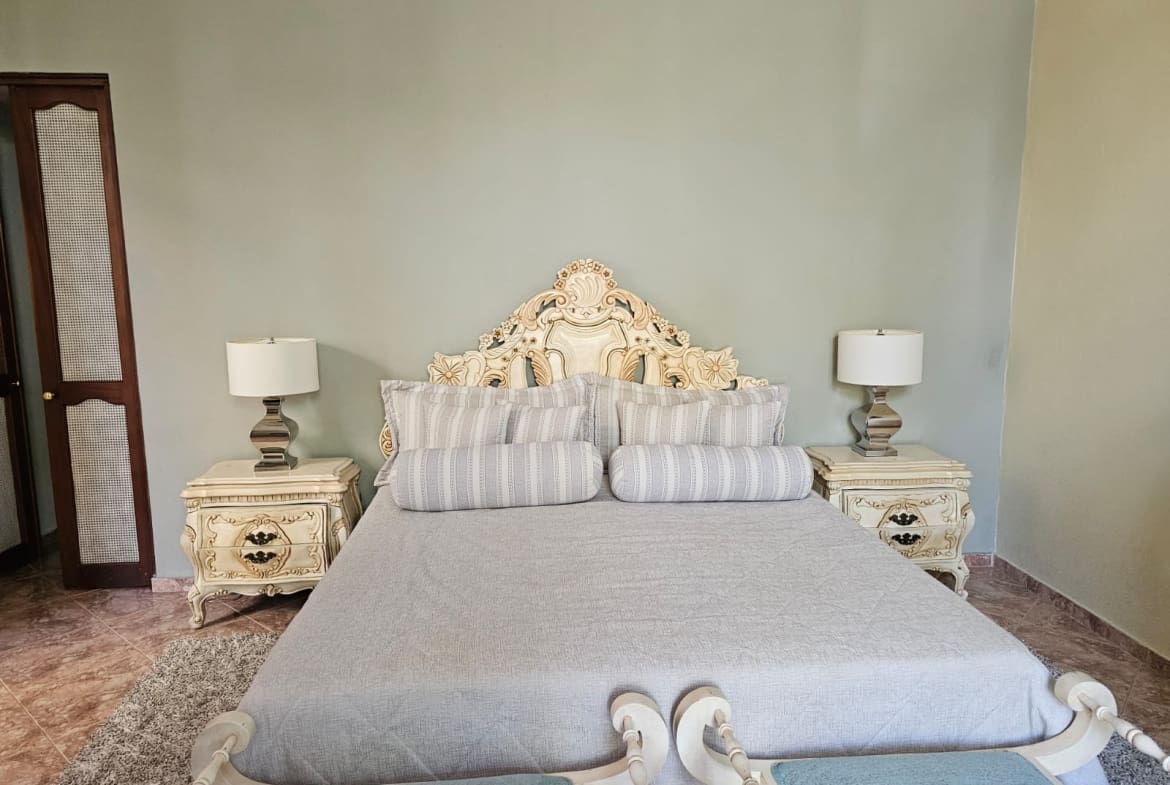 buyDRproperty Luxurious bedroom with a king-size bed, ornate headboard, matching nightstands, and lamps. Sosua Real Estate