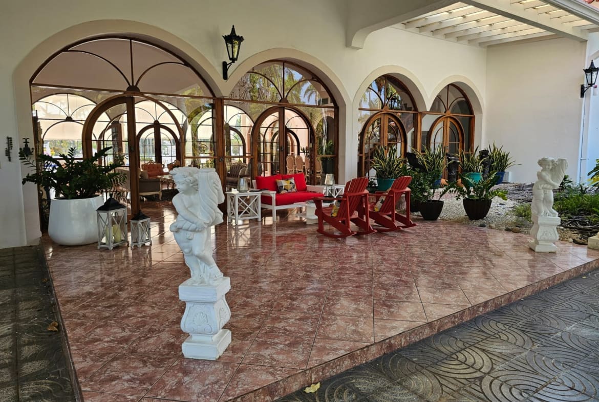 buyDRproperty Elegant patio with arched windows, red chairs, and white statues. Sosua Real Estate