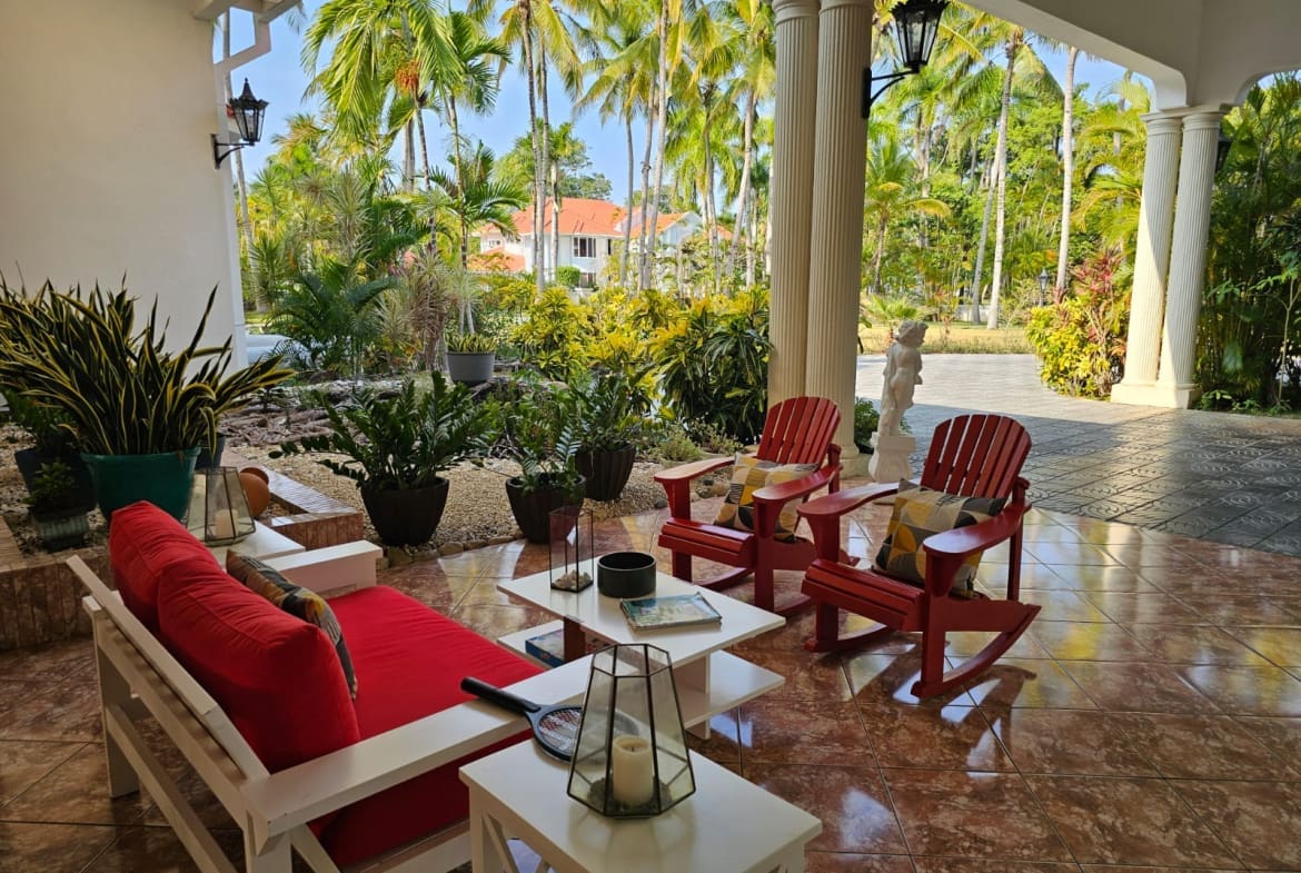 buyDRproperty Red Adirondack chairs and white sofa on a tiled patio with palm trees. Sosua Real Estate