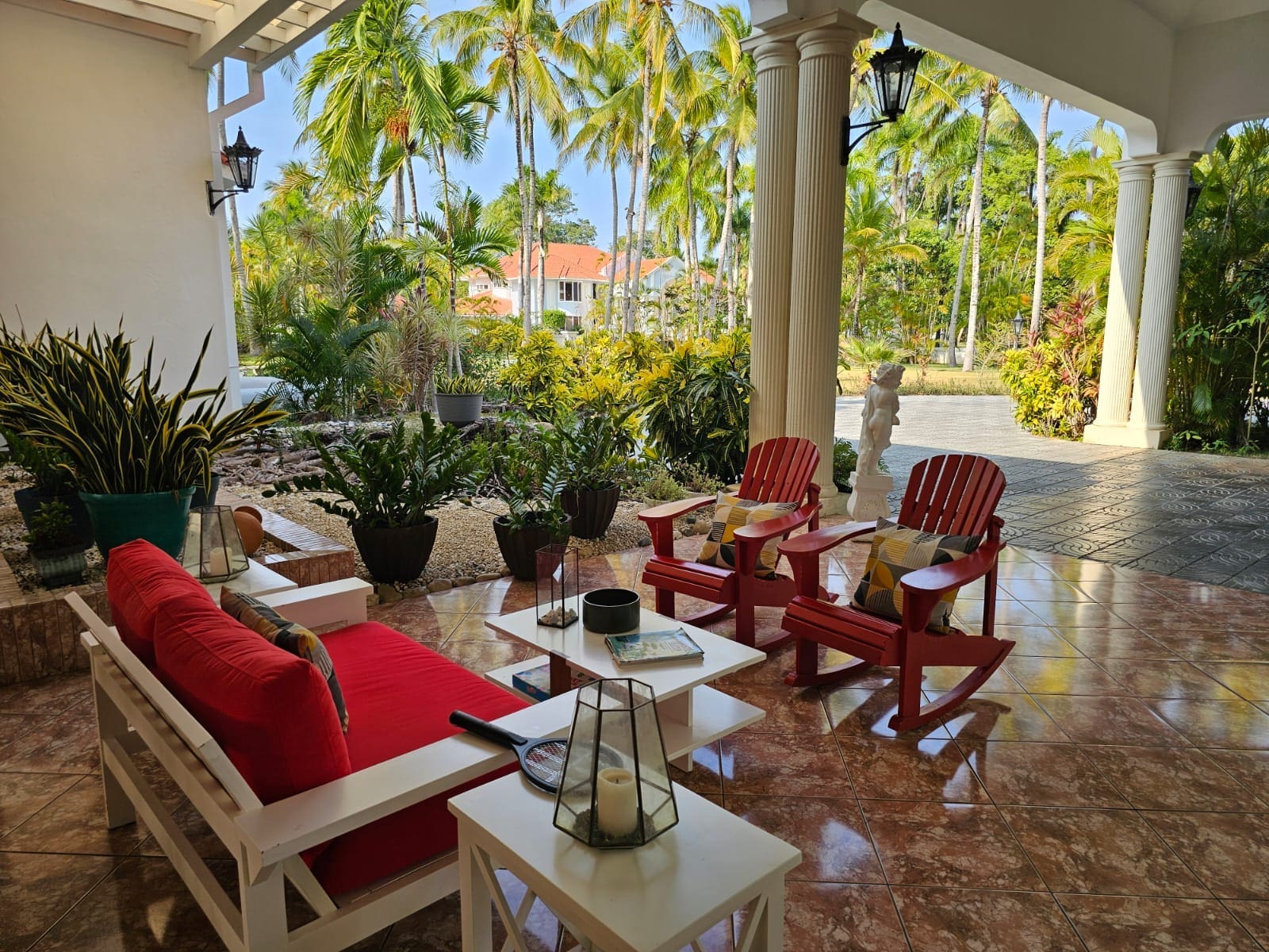 buyDRproperty Red Adirondack chairs and white sofa on a tiled patio with palm trees. Sosua Real Estate