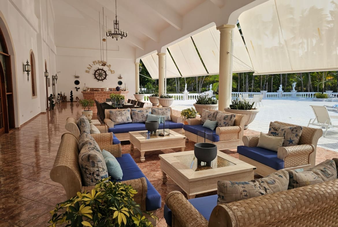 buyDRproperty Tropical patio lounge with wicker furniture, blue cushions, and palm trees Sosua Real Estate