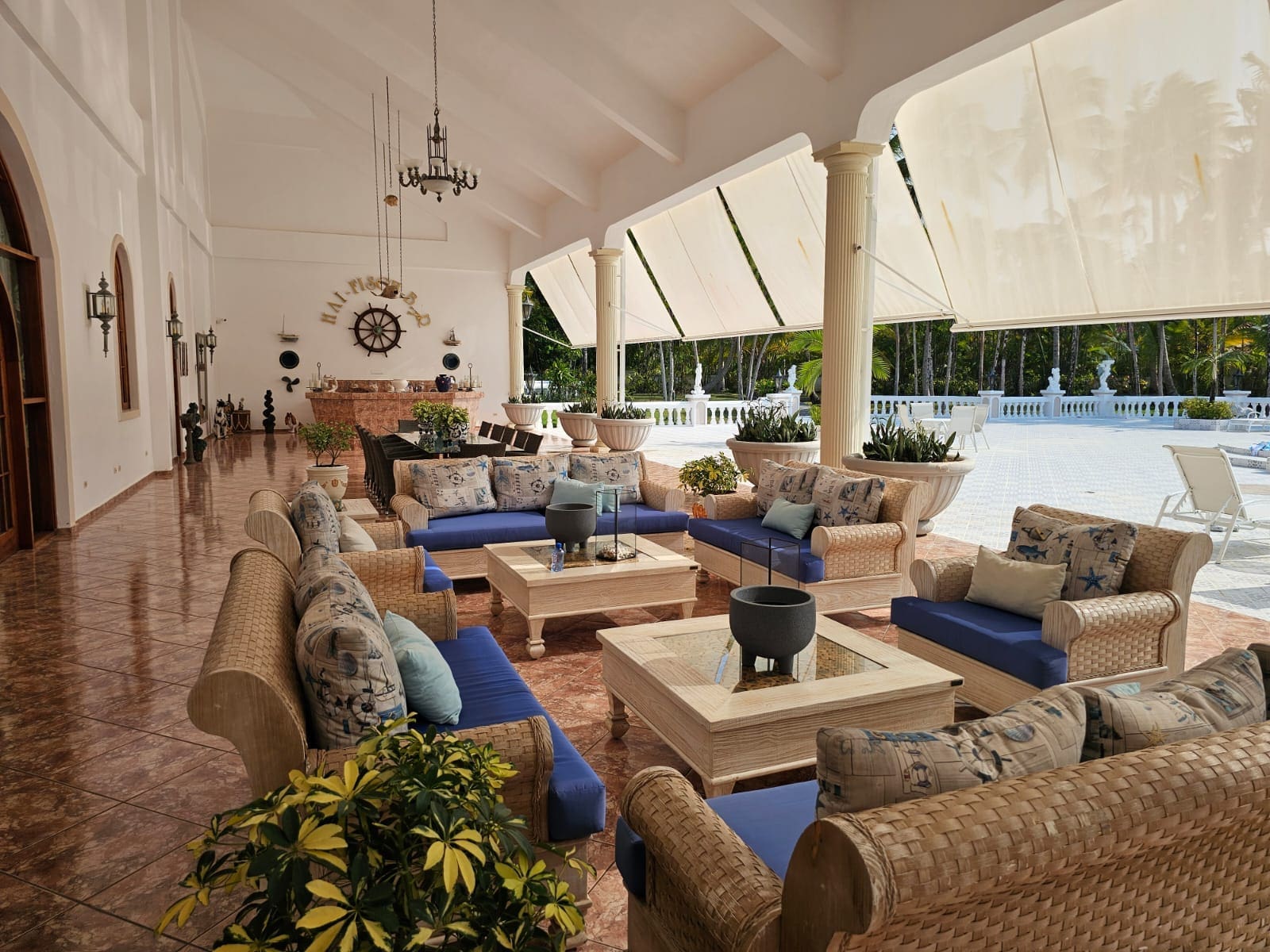 buyDRproperty Tropical patio lounge with wicker furniture, blue cushions, and palm trees Sosua Real Estate