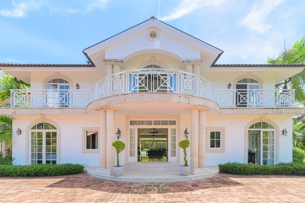 buyDRproperty Luxury white villa with arched windows and a balcony, surrounded by lush greenery. Sosua Real Estate