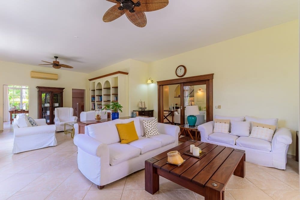 buyDRproperty Spacious, bright living room with white sofas, wooden coffee table, and built-in bookshelves. Sosua Real Estate