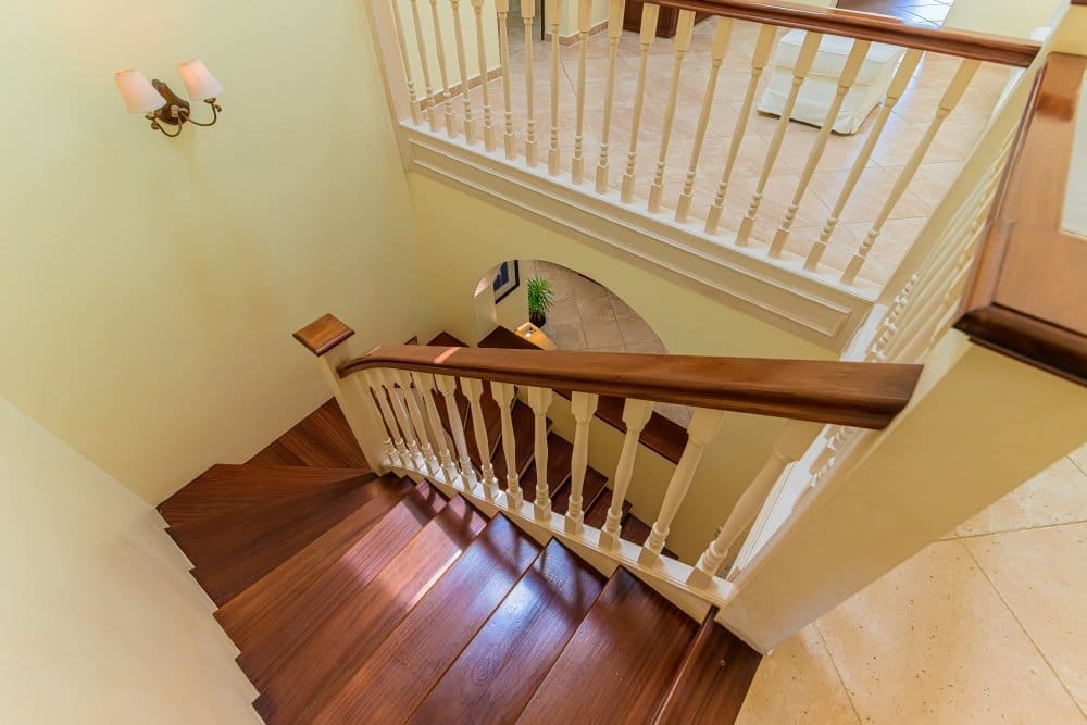 Curved wooden staircase with white spindles and a dark handrail in a pale yellow hallway, view from above.