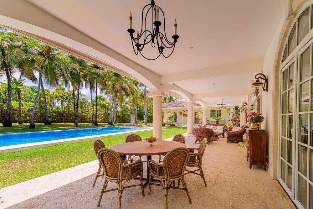buyDRproperty Luxury patio with dining set and chairs overlooking a tropical pool and palm trees. Sosua Real Estate