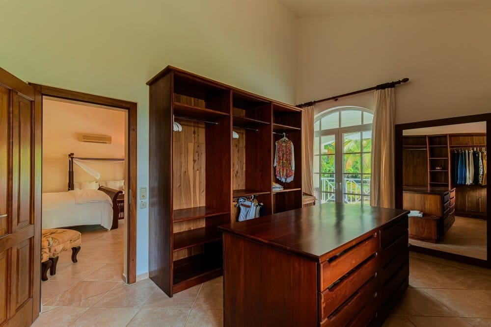 buyDRproperty Spacious walk-in closet with dark wood cabinetry and a king-size bed visible in adjacent room. Sosua Real Estate