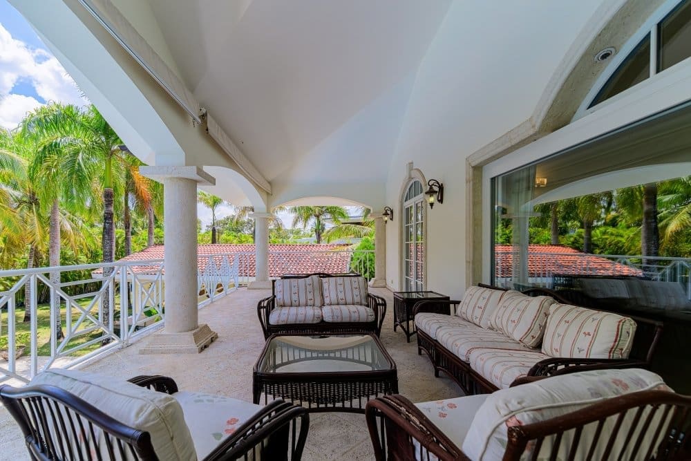 buyDRproperty Spacious covered balcony with wicker furniture, overlooking palm trees and a tiled roof. Sosua Real Estate