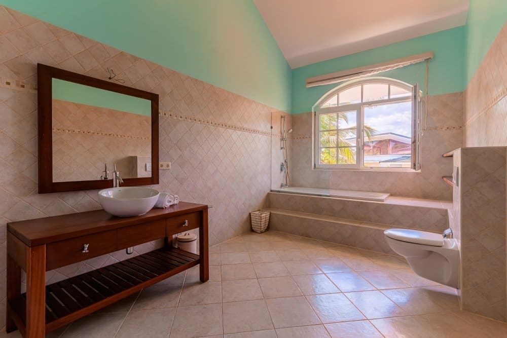 buyDRproperty Spacious bathroom with a wooden vanity, vessel sink, and elevated bathtub near a large arched window. Sosua Real Estate
