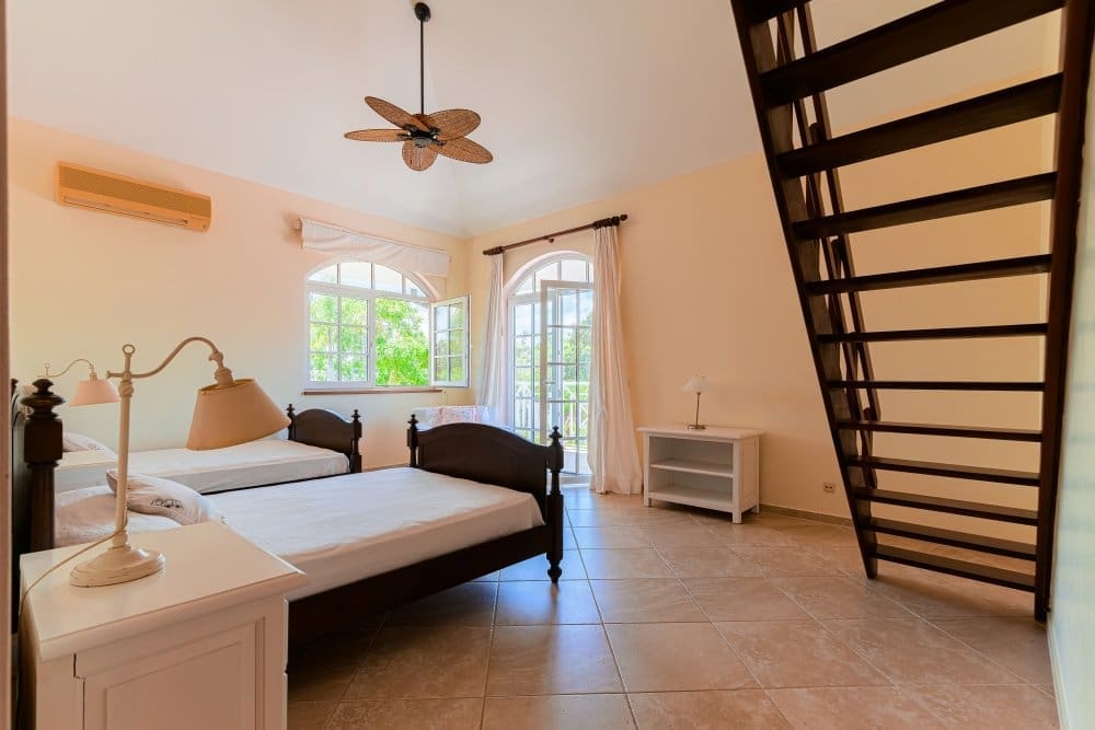 buyDRproperty Bright bedroom with two twin beds, ceiling fan, and stairs leading upstairs. Sosua Real Estate