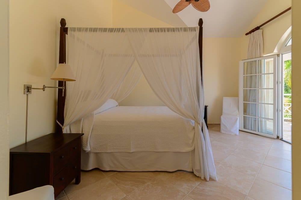 buyDRproperty Four-poster bed with white drapes in a bright, airy bedroom with patio doors Sosua Real Estate