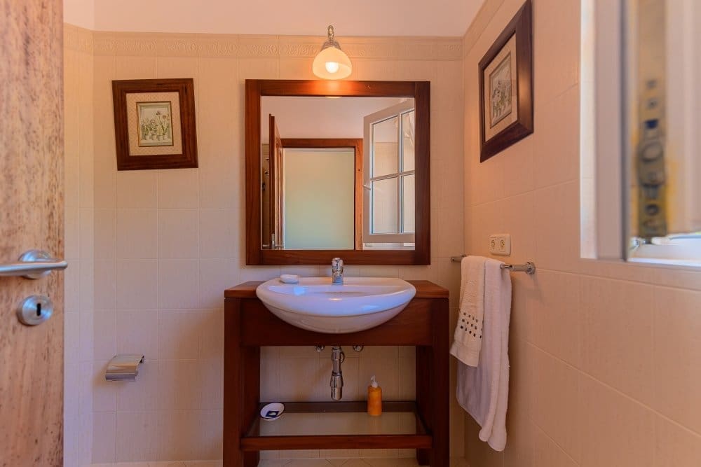 buyDRproperty Modern bathroom vanity with white sink, wooden frame, and tiled walls. Sosua Real Estate