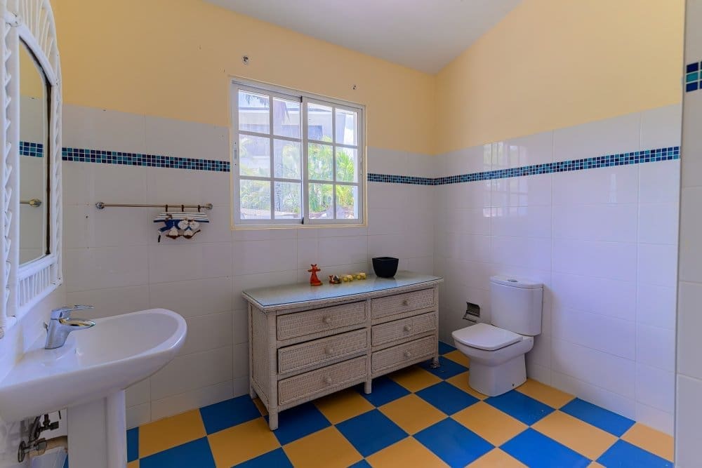 buyDRproperty Bright bathroom with blue and yellow checkered floor, white sink, toilet, and woven dresser. Sosua Real Estate