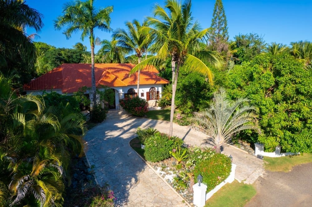 buyDRproperty Tropical villa with red tile roof, palm trees, and lush landscaping. Sosua Real Estate