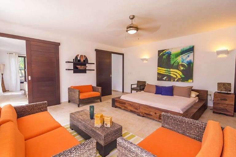 buyDRproperty Modern bedroom with king-size bed, orange seating, and tropical art Sosua Real Estate