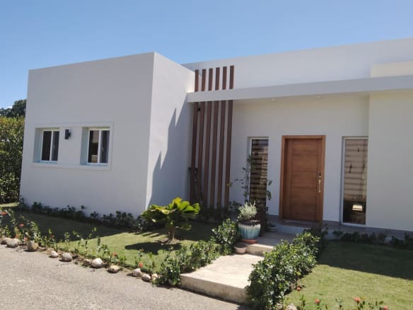buyDRproperty Modern white house exterior with wooden accents and lush landscaping. Sosua Real Estate