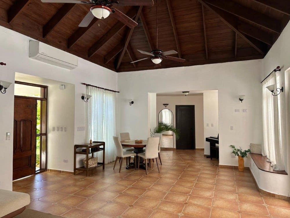 Spacious open-plan living and dining area with a vaulted wooden ceiling, two ceiling fans, and a round dining table with beige chairs.