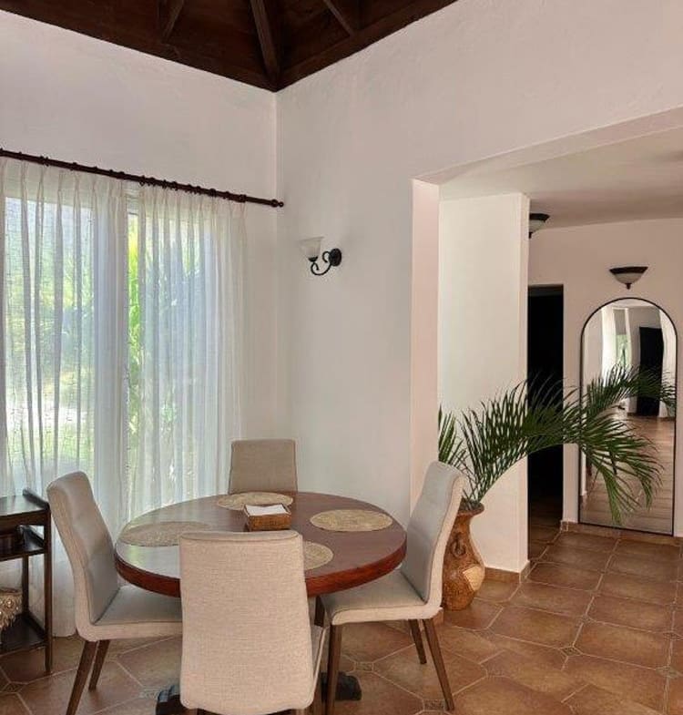 buyDRproperty Round dining table with chairs in a bright room with large windows and tiled floors. Sosua Real Estate
