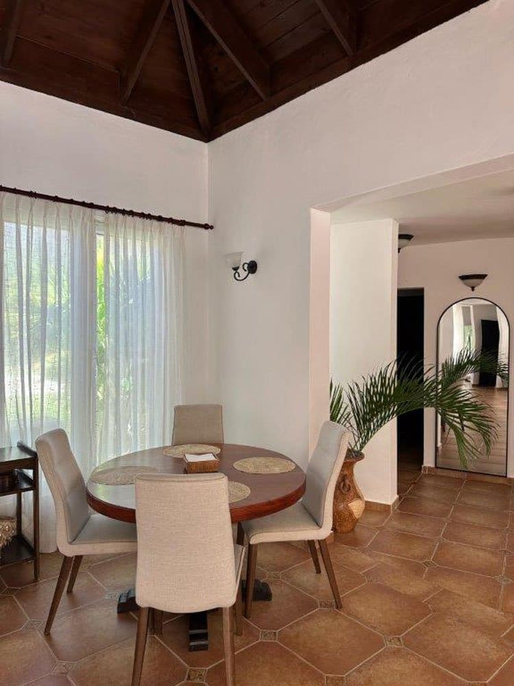 buyDRproperty Round dining table with chairs in a bright room with large windows and tiled floors. Sosua Real Estate