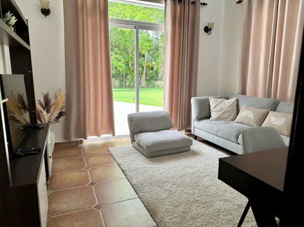 buyDRproperty Cozy living room with gray sofa, floor chair, and large window overlooking greenery Sosua Real Estate