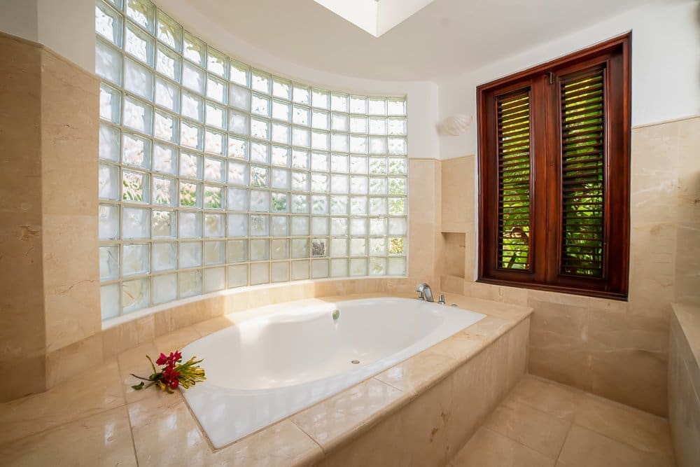 buyDRproperty Luxurious bathroom with a large soaking tub, curved glass block wall, and wooden shutters. Sosua Real Estate