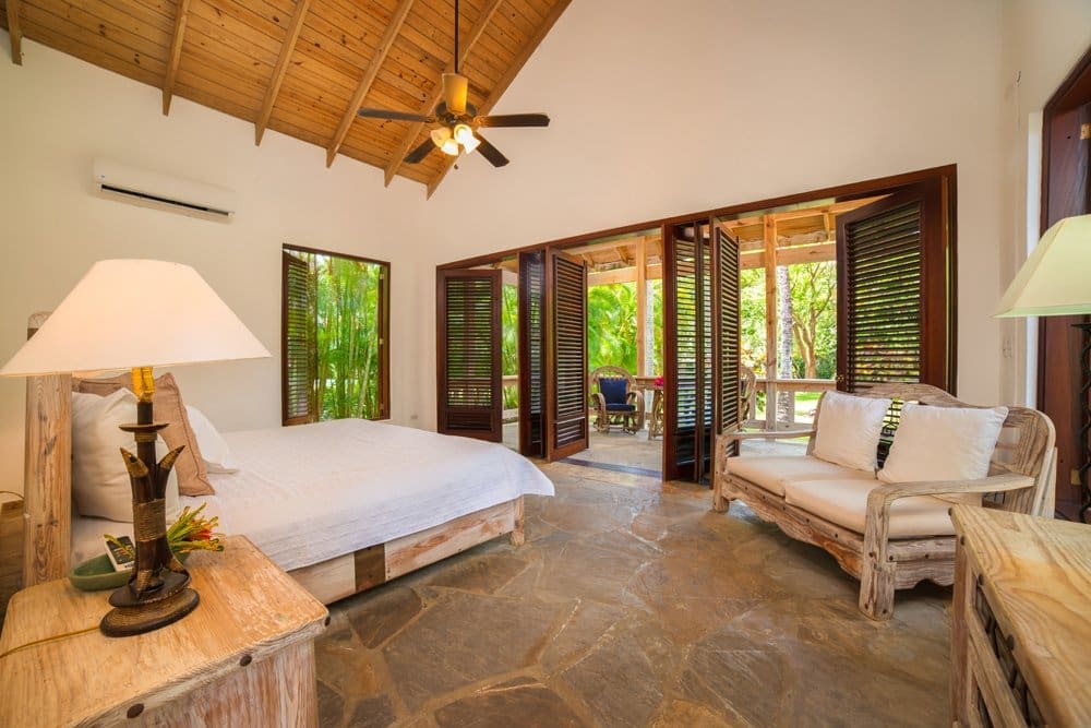 buyDRproperty Tropical bedroom with open shutters, king bed, and rattan sofa Sosua Real Estate